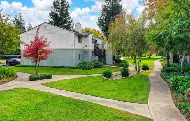 Community grounds with pedestrian walk paths surrounded by mature trees, green grass and shrubs. at Monte Bello Apartments, California, 95826