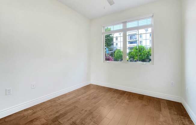 an empty living room with a window and wooden floors