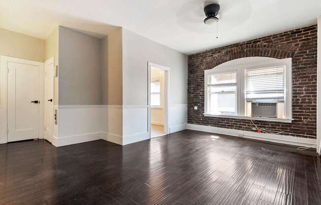 A living room with a brick wall and wooden floors leading into a kitchen at Brookmore Apartments.