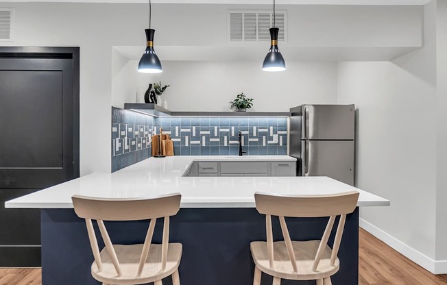 A modern kitchen with a white island and two chairs.