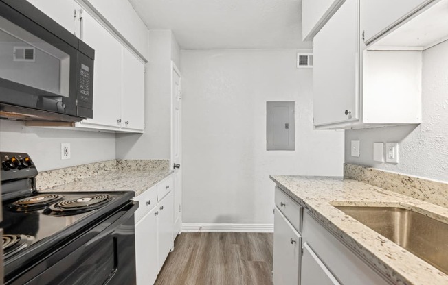 a renovated kitchen with white cabinets and granite counter tops and black appliances