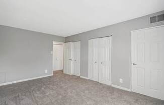 A room with grey walls and carpeted floor with three white doors.
