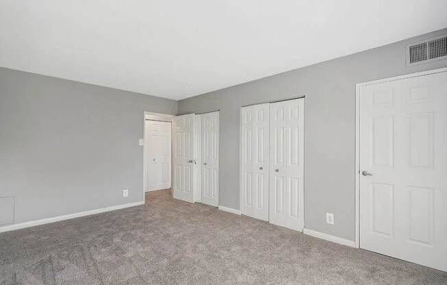 A room with grey walls and carpeted floor with three white doors.