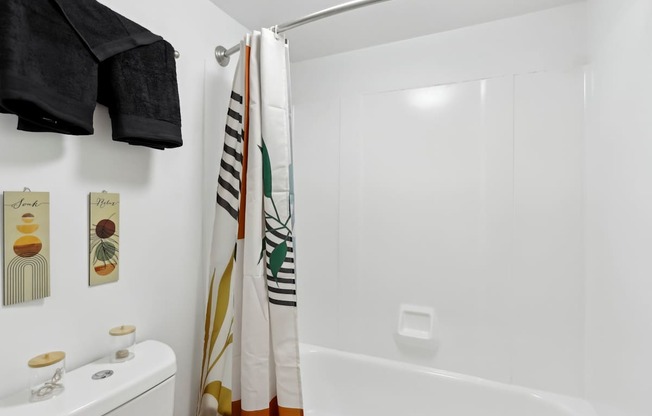 A white bathroom with a toilet, a shower curtain, and a towel rack.