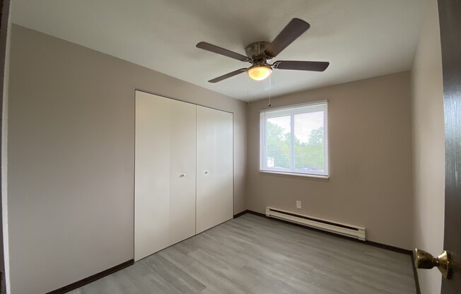 an empty bedroom with a ceiling fan and a closet