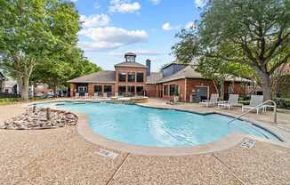 A pool with a stone border and a building in the background.