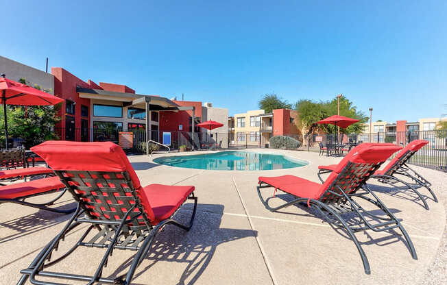 A pool area with red chairs and a red umbrella.