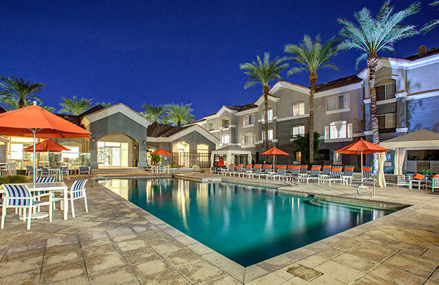 The Highland Apartments Pool as sunset with lounge seating, umbrellas, and palm trees