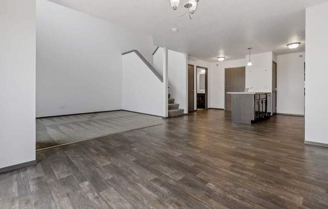 A spacious room with wooden flooring and a kitchen area in the background.