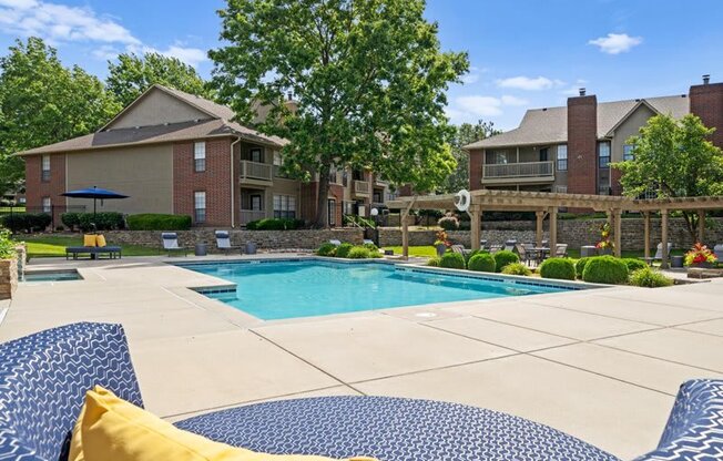 a swimming pool with blue and white chairs and a house in the background at Highland Park Apartment Homes, Overland Park