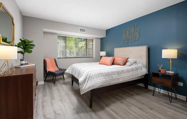 A bedroom with a bed, chair, and a plant.