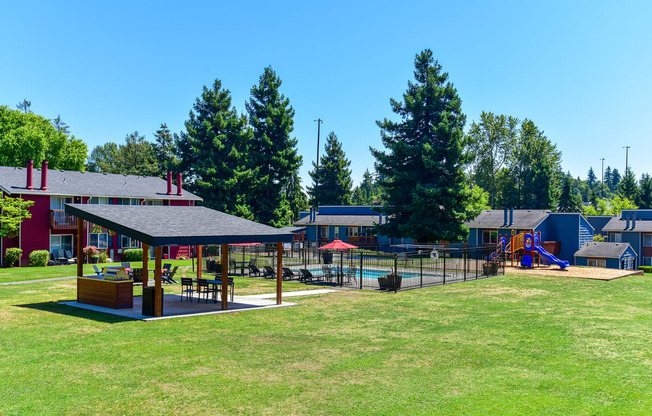 a large grassy area with a playground and buildings in the background