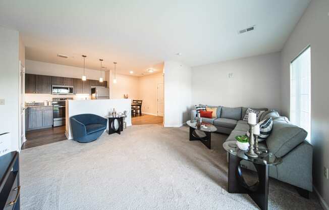 Living room leading into kitchen, blue chair next to island countertop, couch to the right in the corner, light tan carpet.