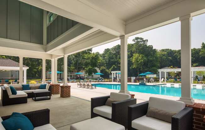 a covered patio with couches and chairs and a pool in the background