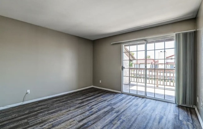 an empty living room with a sliding glass door to a balcony