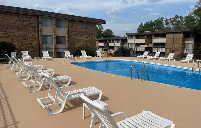 A row of white chairs are lined up on a tan pool deck.