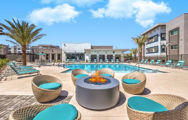 uxurious apartment complex showcasing a stylish outdoor pool area with cozy wicker seating and a modern fire pit, surrounded by palm trees under a clear blue sky.