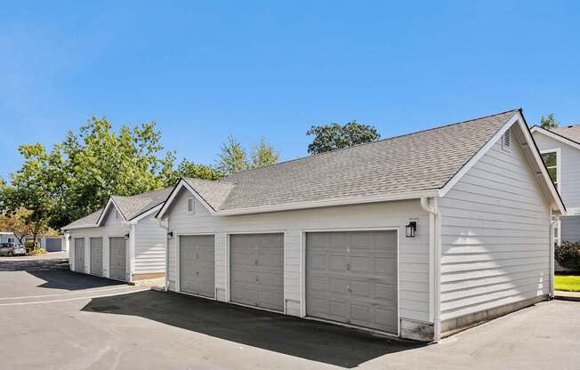A row of white garages with grey doors are lined up in a parking lot.