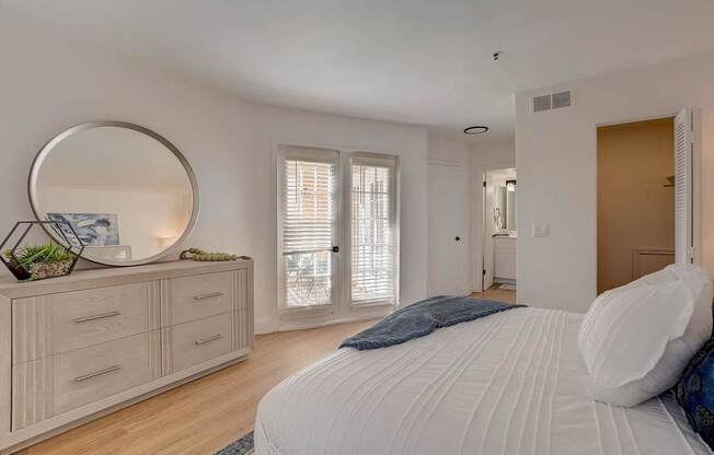 A bedroom with a large bed, a dresser with a mirror, and a window with blinds.