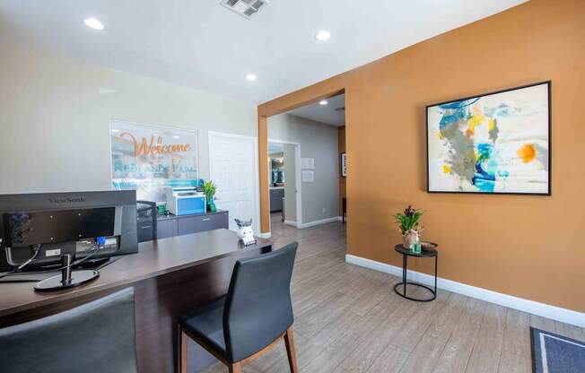 A room with a desk, chair, and a painting on the wall.
