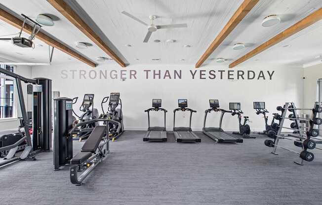 A gym with a variety of equipment and a sign that says "STRONGER THAN YESTERDAY".
