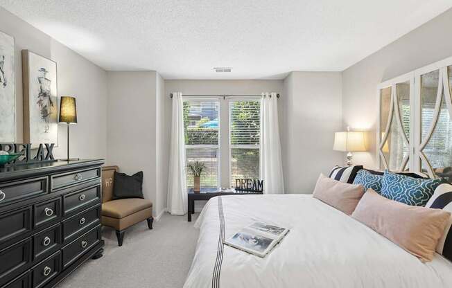 A bedroom with a large bed, a dresser, and a window with a view of the city.