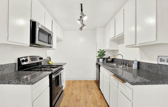 a kitchen with marble counter tops and white cabinets at Casa Del Amo Apartments, Torrance California