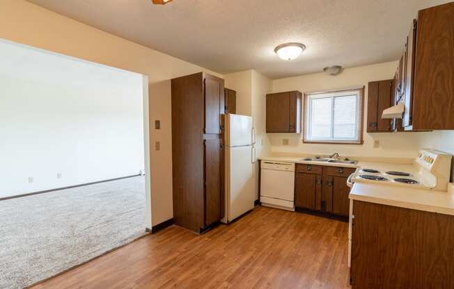 Kitchen with white appliances and brown cabinets a small window above the sink brightens the room with natural light at Parkwest Gardens West Fargo, ND