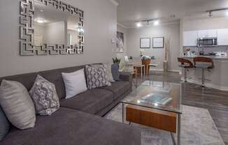 A living room with a grey couch and a mirror on the wall.