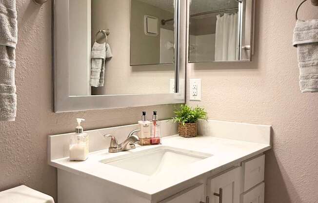 A white bathroom with a toilet, sink, mirror and towel rack.