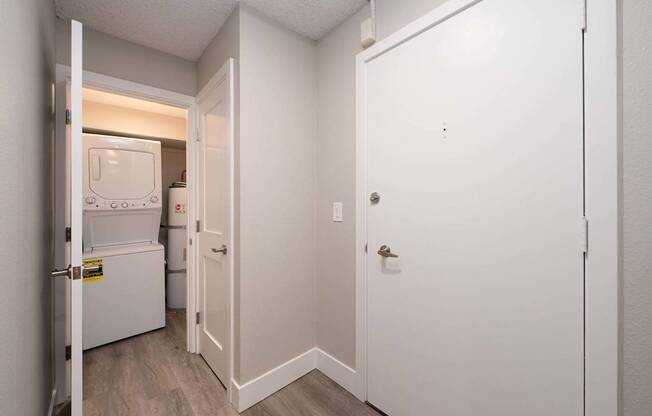 A white door is open to a small kitchen with a refrigerator and a microwave.