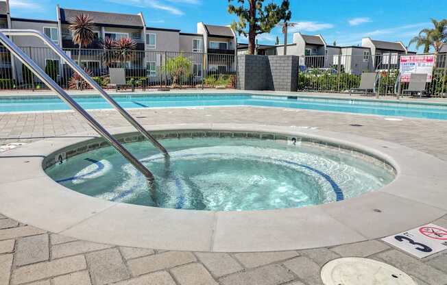 A hot tub in the middle of a brick patio with a pool in the background.