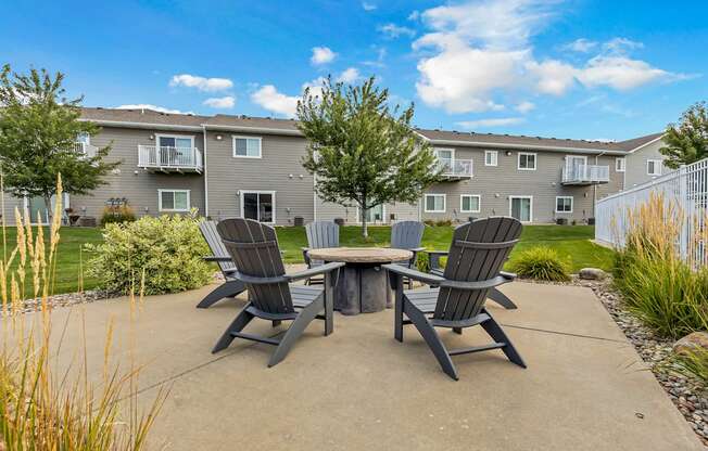 A concrete patio with a table and chairs in front of a grey apartment building.