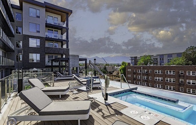 A modern apartment complex with a pool and sun loungers.