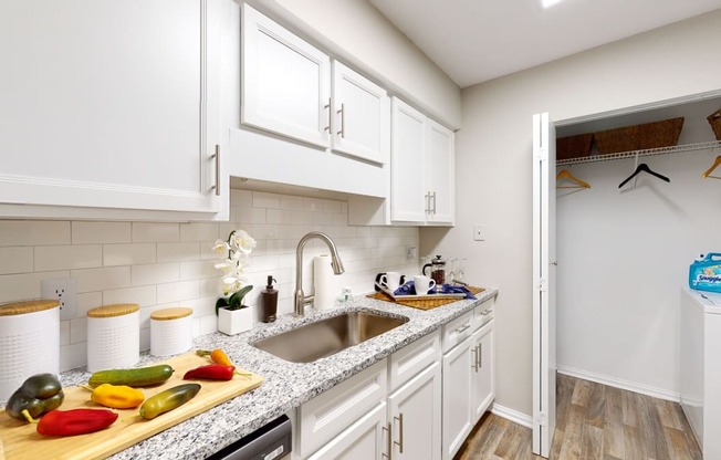 a kitchen with white cabinets and a wooden cutting board with vegetables on it