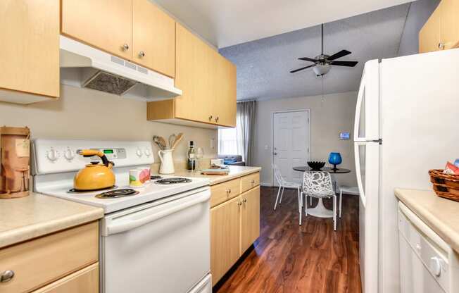 Model home kitchen with hardwood inspired flooring , white kitchen appliances, and dining area with ceiling fan.