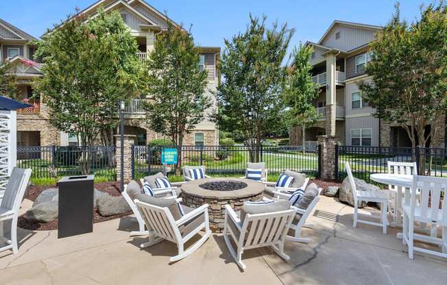 A patio with white chairs and a fire pit in front of apartment buildings.