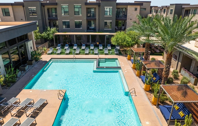 A swimming pool surrounded by sun loungers and palm trees.