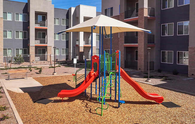 A playground with a red slide and a white umbrella.
