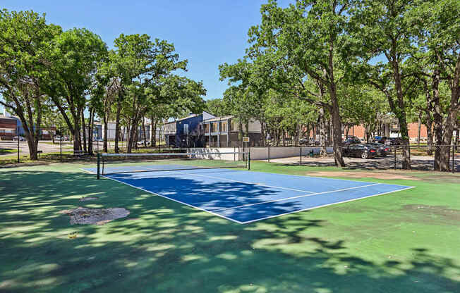 A blue and green tennis court surrounded by trees.