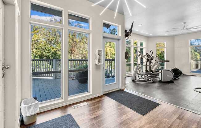 A spacious room with a gym setup and a view of a deck through the sliding glass doors.