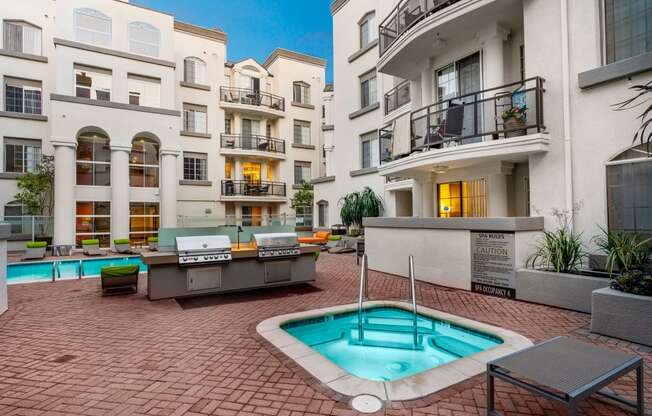 Miracle Mile, Los Angeles, CA Apartments - The Preston Miracle Mile - Resort-Inspired Pool Area With A Sparkling Pool, Hot Tub, Lounge Chairs, Umbrellas, And Two BBQ Grilling Stations