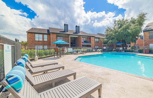 A pool area with sun loungers and a building in the background.