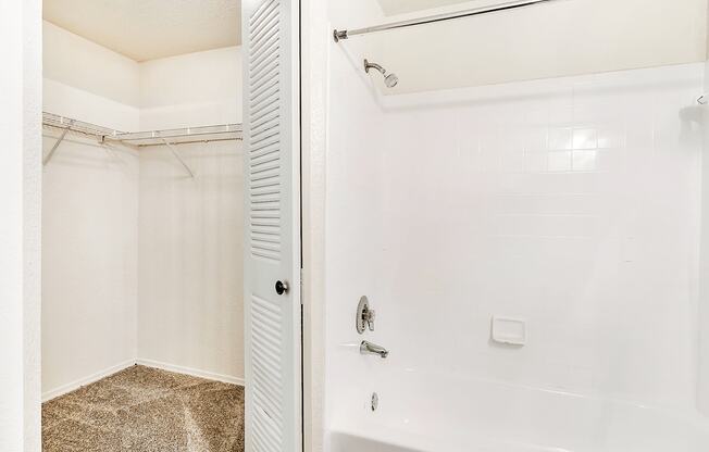 Carpeted walk in closet inside of the bathroom next to the tub with white tile and chrome finishes