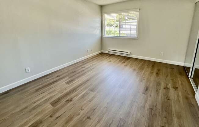 an empty living room with wood flooring and a window