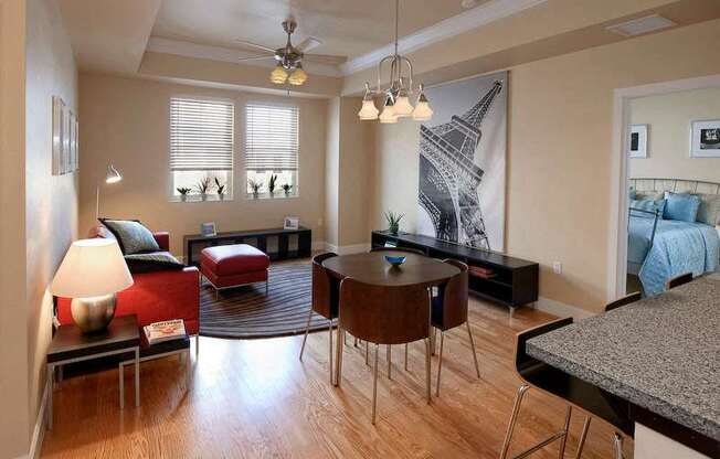 A living room with two windows, a ceiling fan, and hardwood-style flooring near a bedroom and open access to a kitchen.