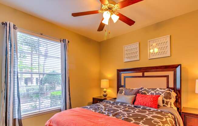 a bedroom with a large window and a ceiling fan