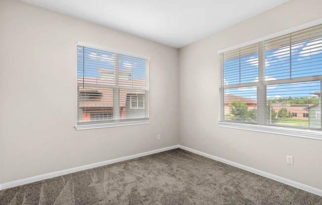 an empty bedroom with two windows and carpeting at Switchback on Platte Apartments, Littleton, CO