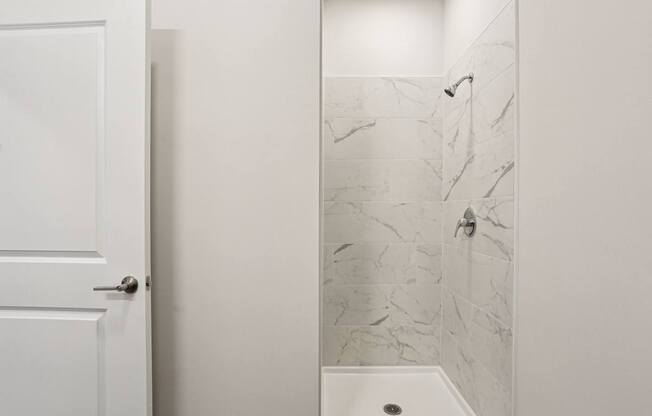 A white door is open to a bathroom with a marble shower.