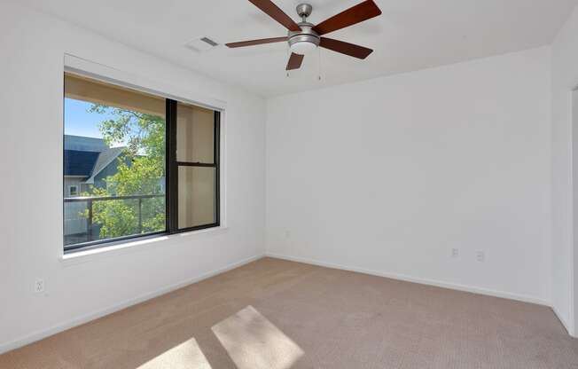 an empty living room with a ceiling fan and a large window